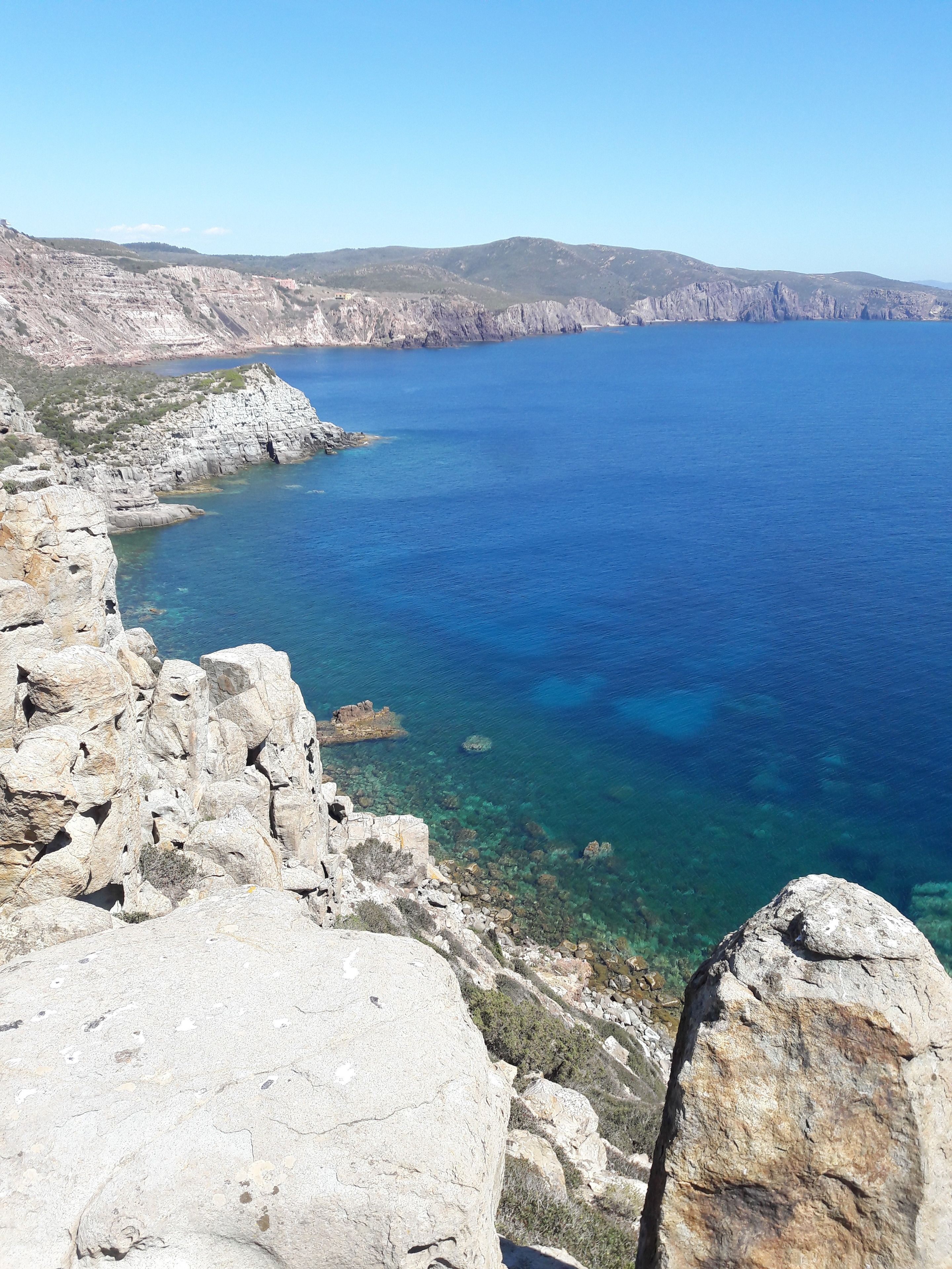 A coastal landscape with rocky cliffs and clear blue sea.