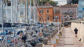 Un port de plaisance où sont amarrés de nombreux bateaux, une promenade piétonne et des bâtiments en arrière-plan.