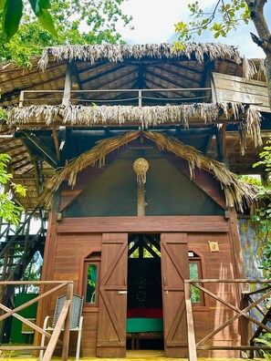Une cabane en bois perchée dans un arbre, avec un toit de chaume, plusieurs niveaux et un ornement suspendu au centre.