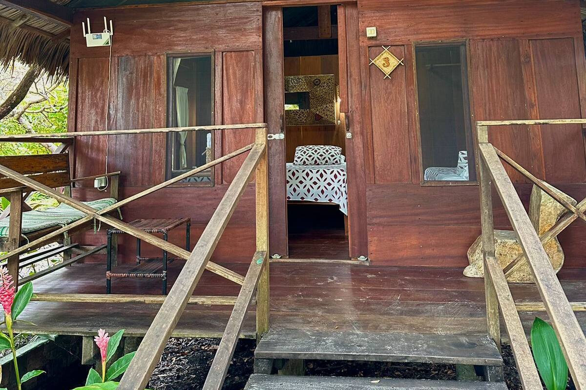 Une cabane en bois avec un toit de chaume, un escalier menant à l’entrée et un petit porche.
