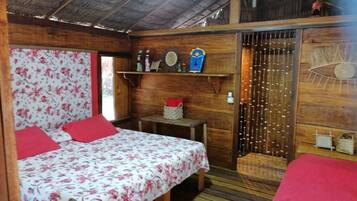 A wooden room with a bed, a small table, and a shelf with decorative items.