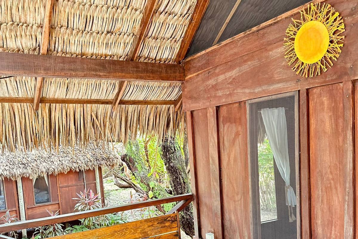 Un banc en bois avec des coussins jaunes, un toit de chaume et un mur en bois orné d’une fenêtre et d’une décoration représentant un soleil.