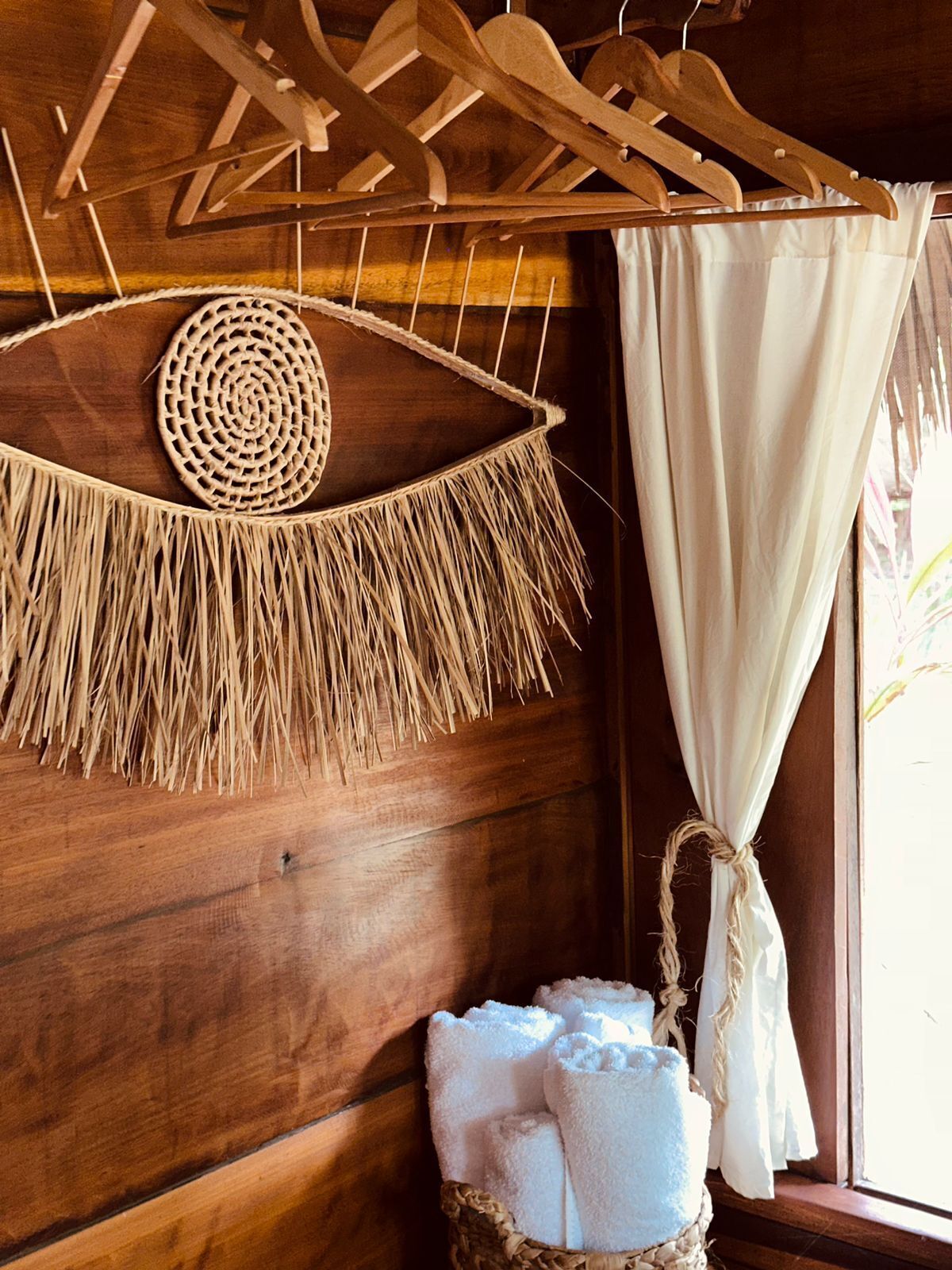 A wooden room with a macrame wall hanging, a woven basket with towels, and a wooden ceiling with a wooden hanger.