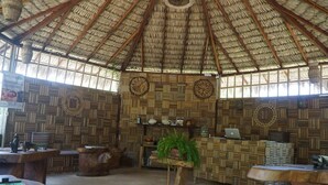 A room with a thatched roof, woven wooden walls, and a central table with a plant. - Ciamat Camp (Santo Amaro do Maranhão)