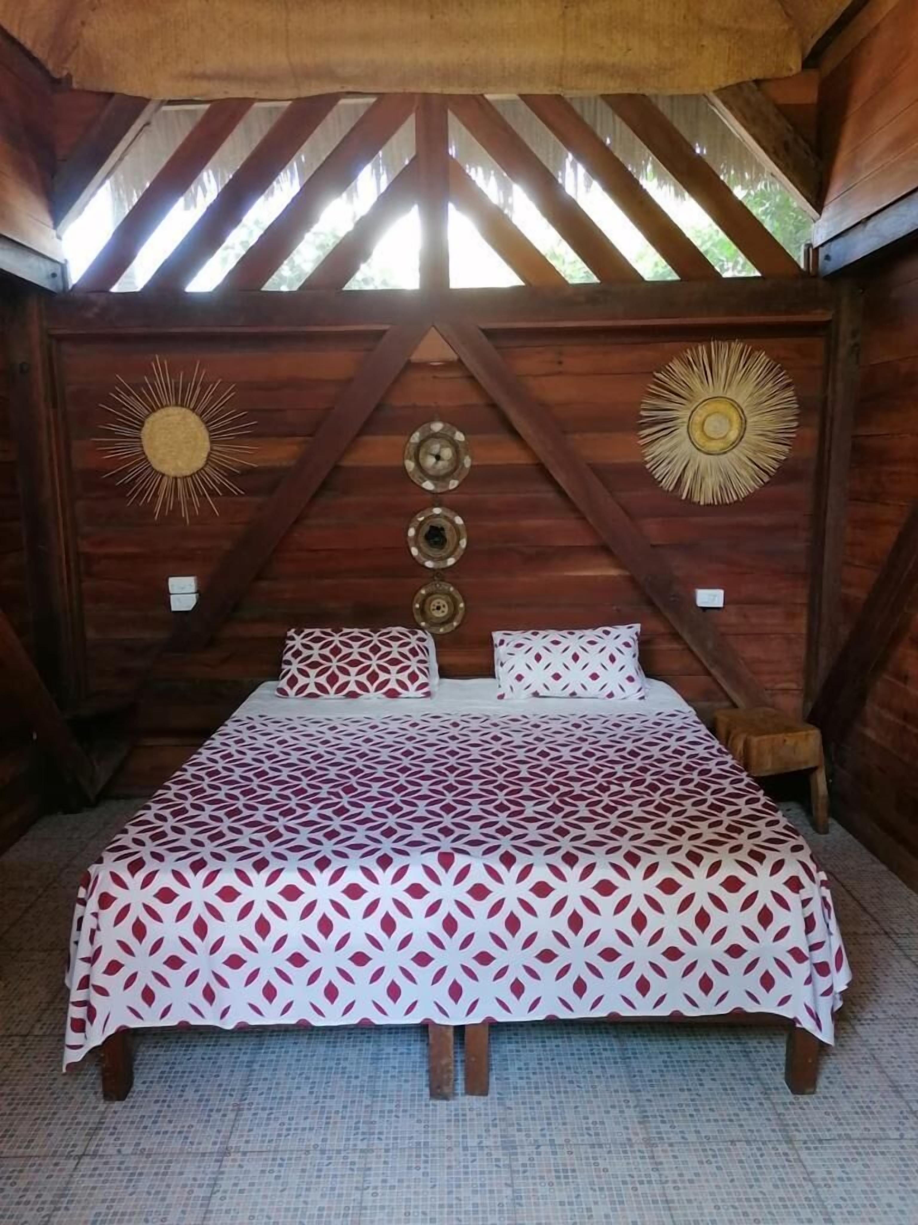 Ein Bett mit einem geometrisch gemusterten Überwurf in einem rustikalen Zimmer mit Holzbalken und Wanddekoration.