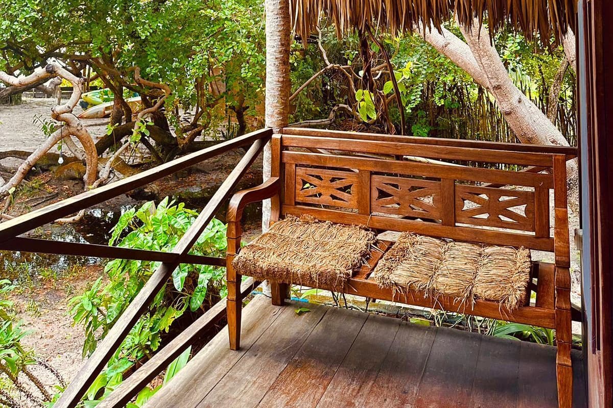 Un banc en bois, placé sous une structure à toit de chaume, offre une vue sur une végétation luxuriante.