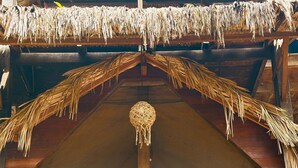 A wooden building with a thatched roof, a central pole, and a door with a green and red cloth. - Ciamat Camp (Santo Amaro do Maranhão)