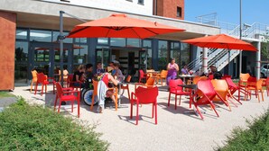 An outdoor seating area with red chairs and orange umbrellas, a staircase, and a building with large windows.