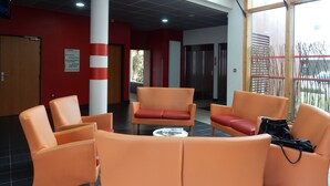 A lobby with orange chairs, a white pillar, and an elevator.