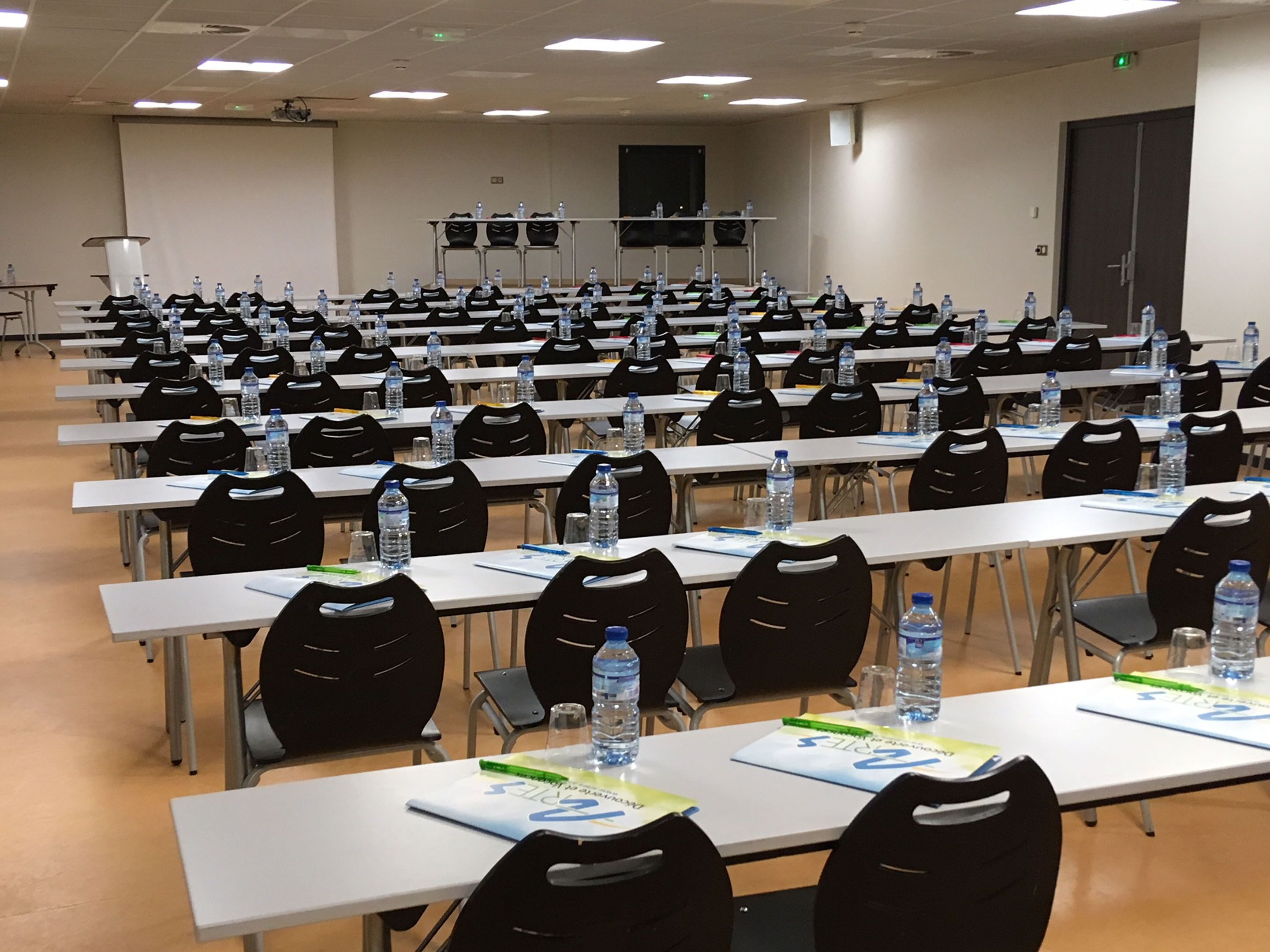 Una sala de conferències amb files de taules, cadires i ampolles d'aigua.