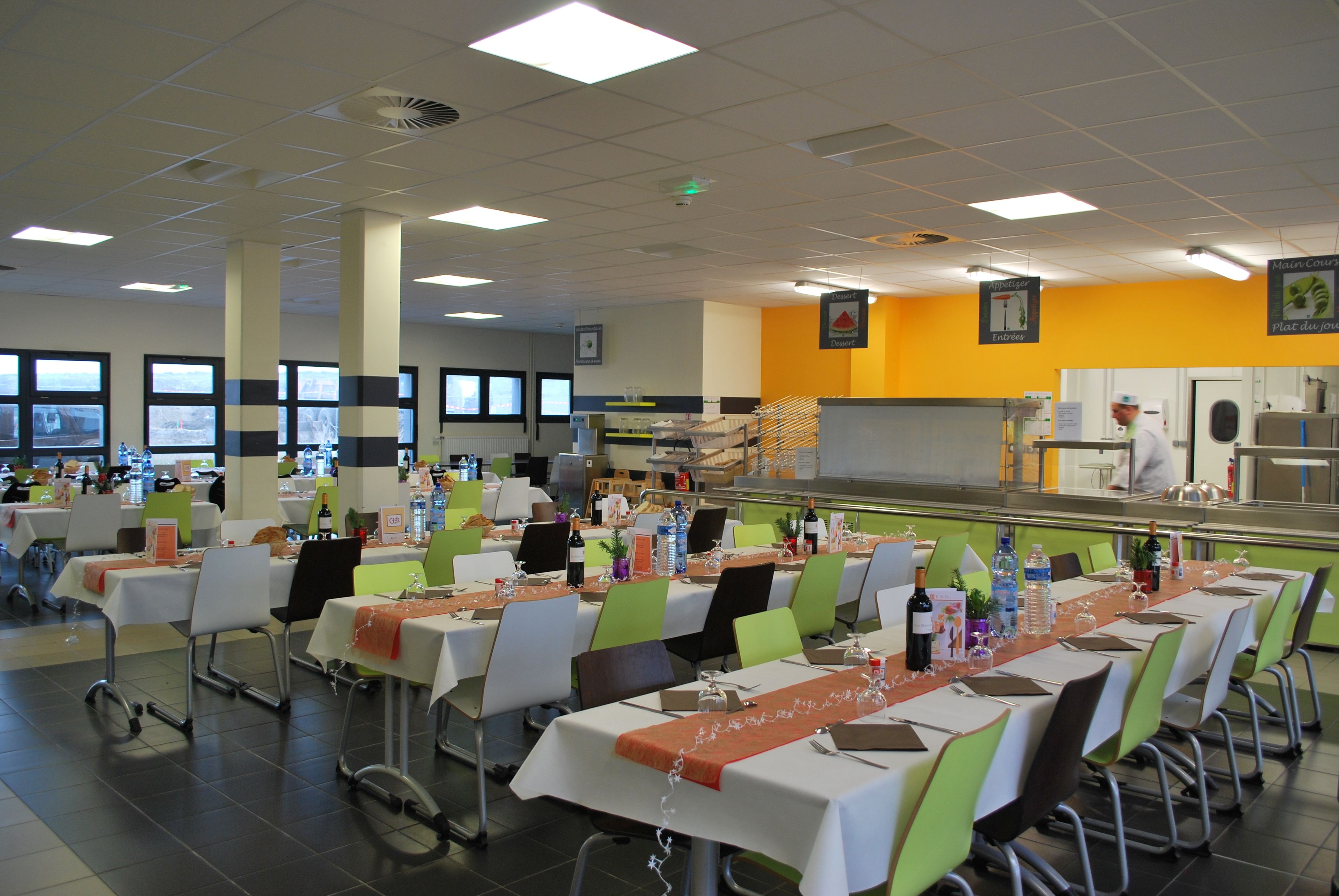 A cafeteria with multiple tables, chairs, and a kitchen area.