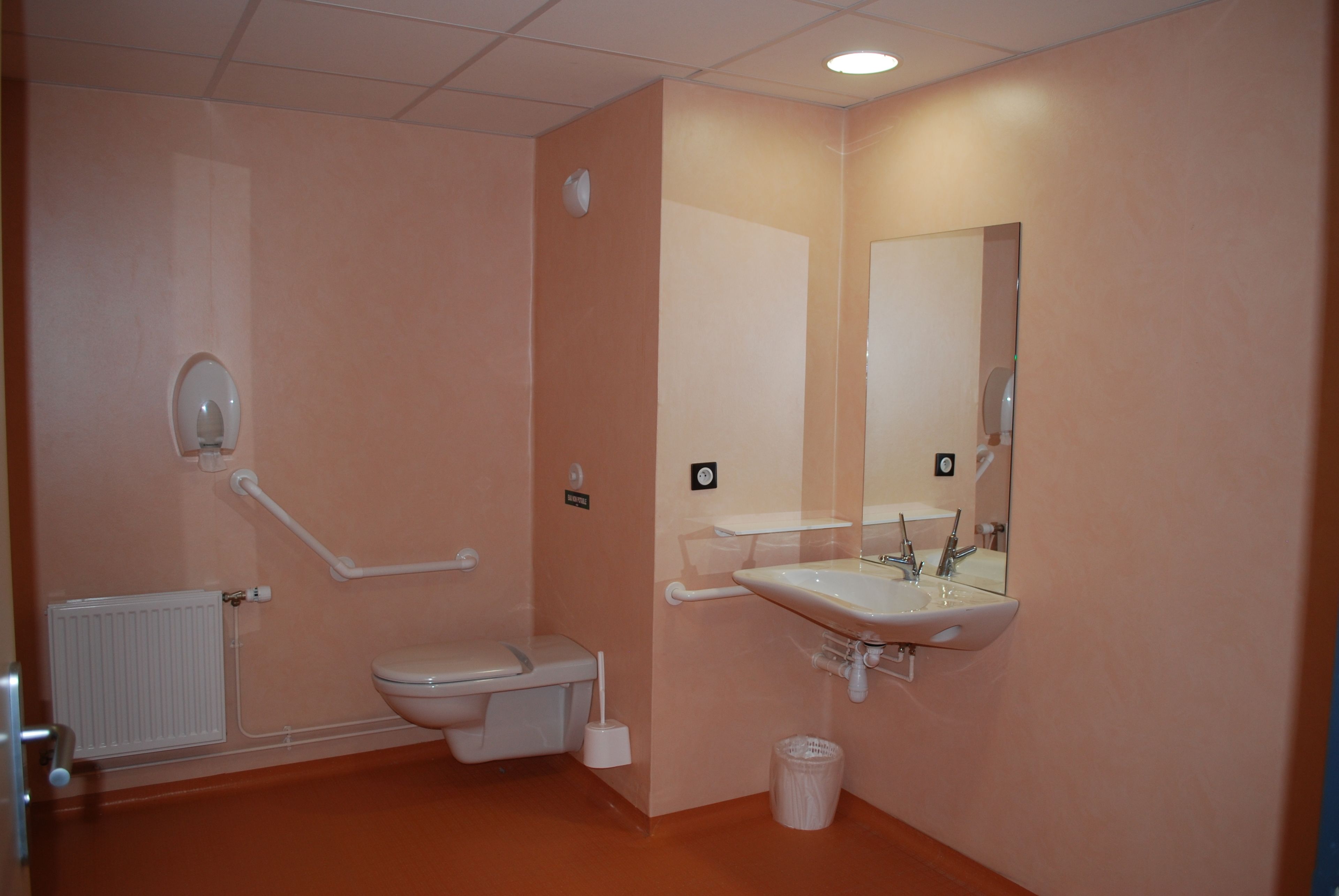A bathroom with a toilet, bidet, sink, mirror, and hand dryer.