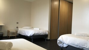 A modern hotel room with two beds, a wooden wardrobe, and a small bedside table.