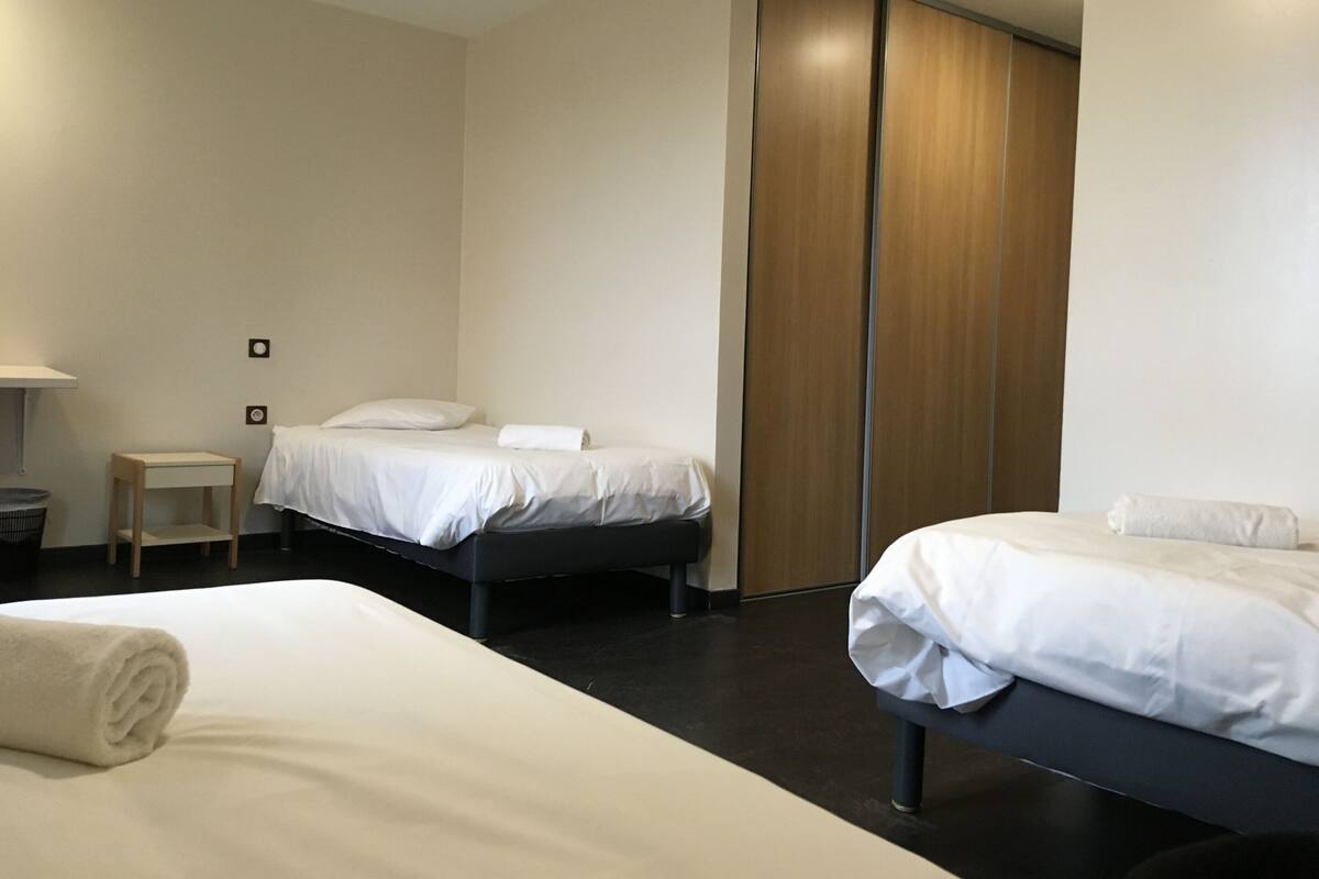 A modern hotel room with two beds, a wooden wardrobe, and a small bedside table.