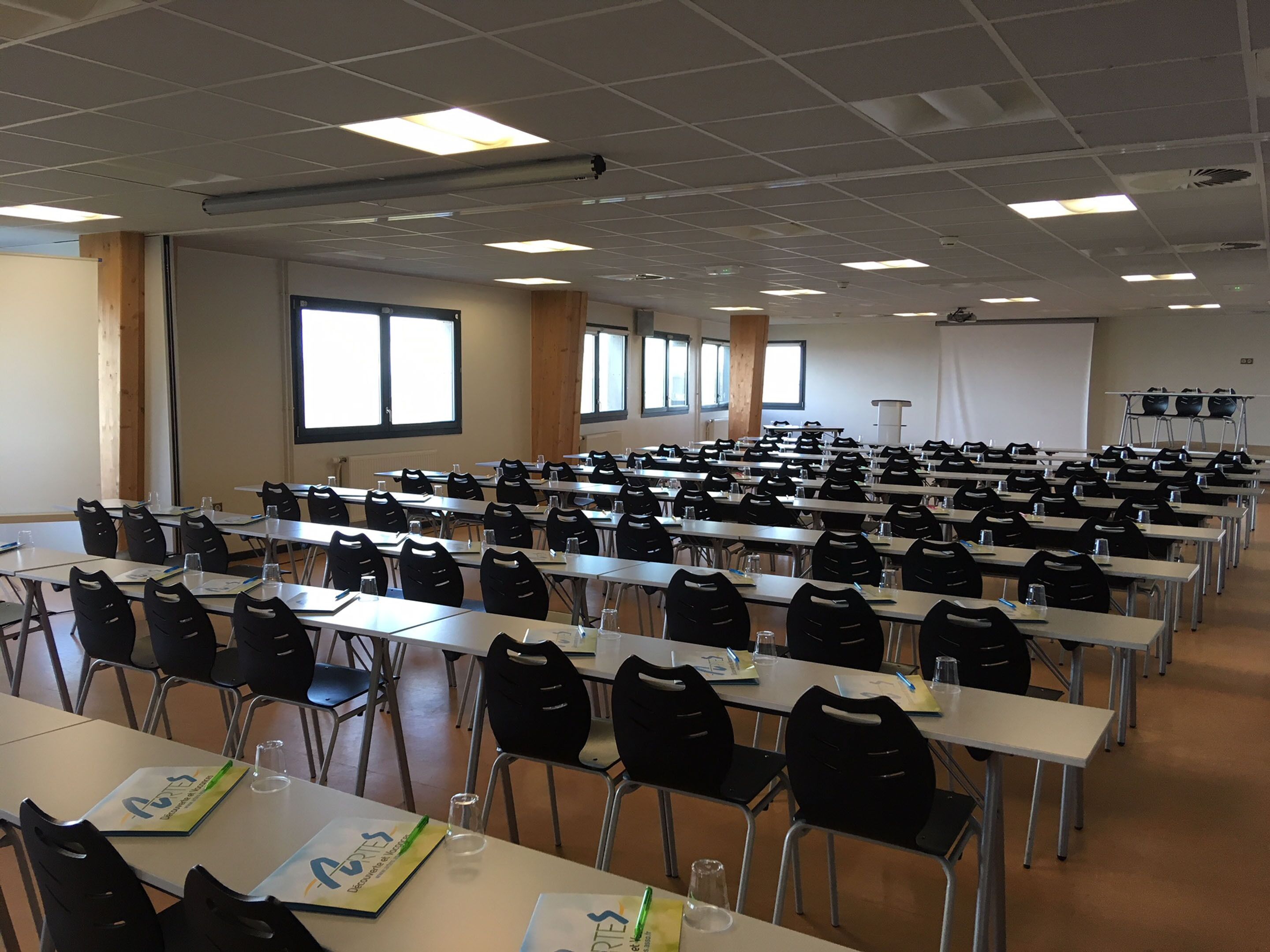 A conference room with rows of tables and chairs, large windows, and a whiteboard.
