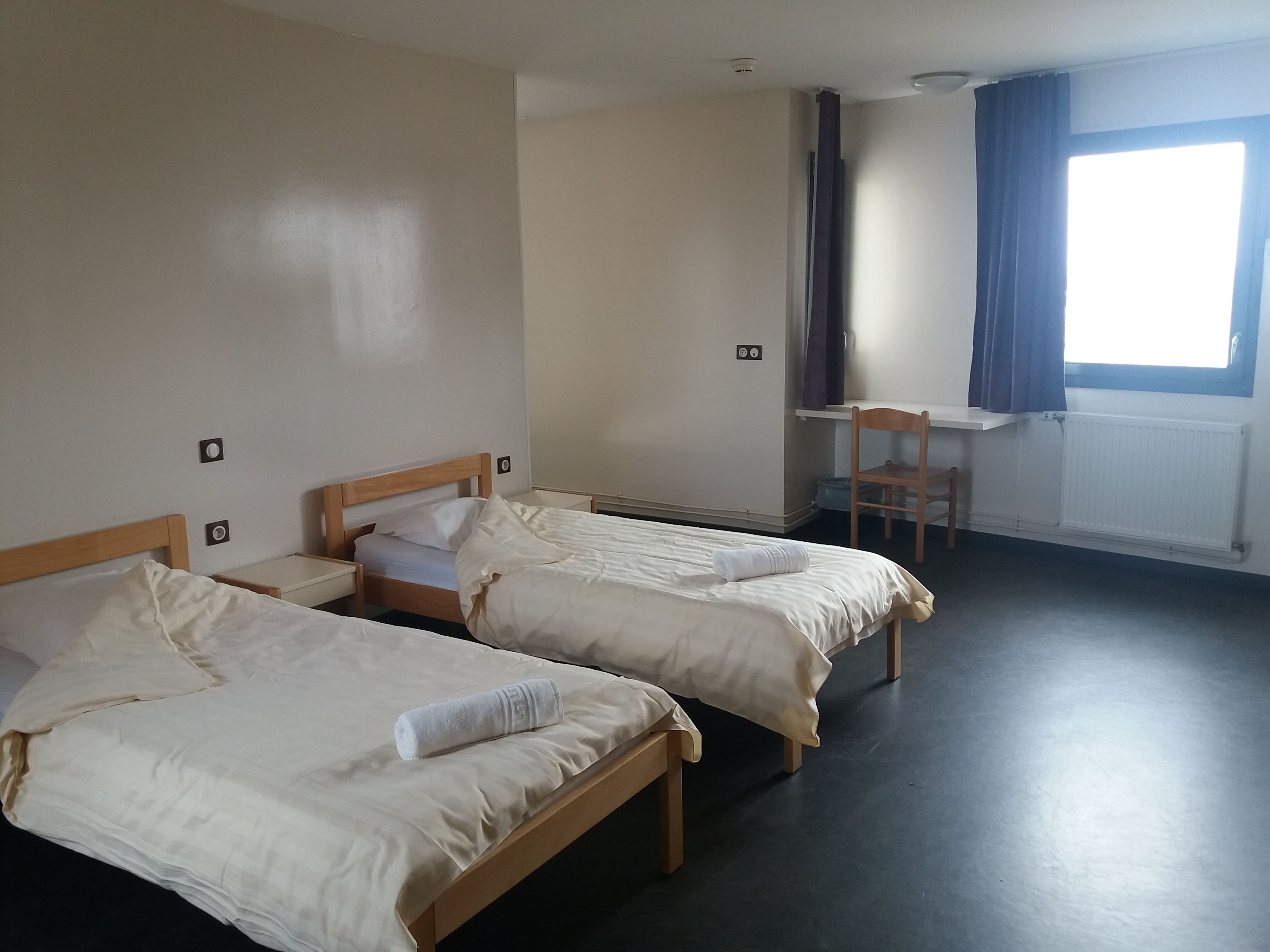 Une chambre d’hôtel avec deux lits simples, un bureau et une chaise.