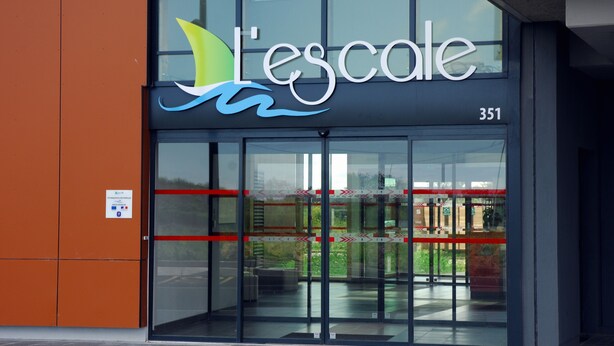 A building with a large glass entrance, a sign reading "L'escole," and the number 351.