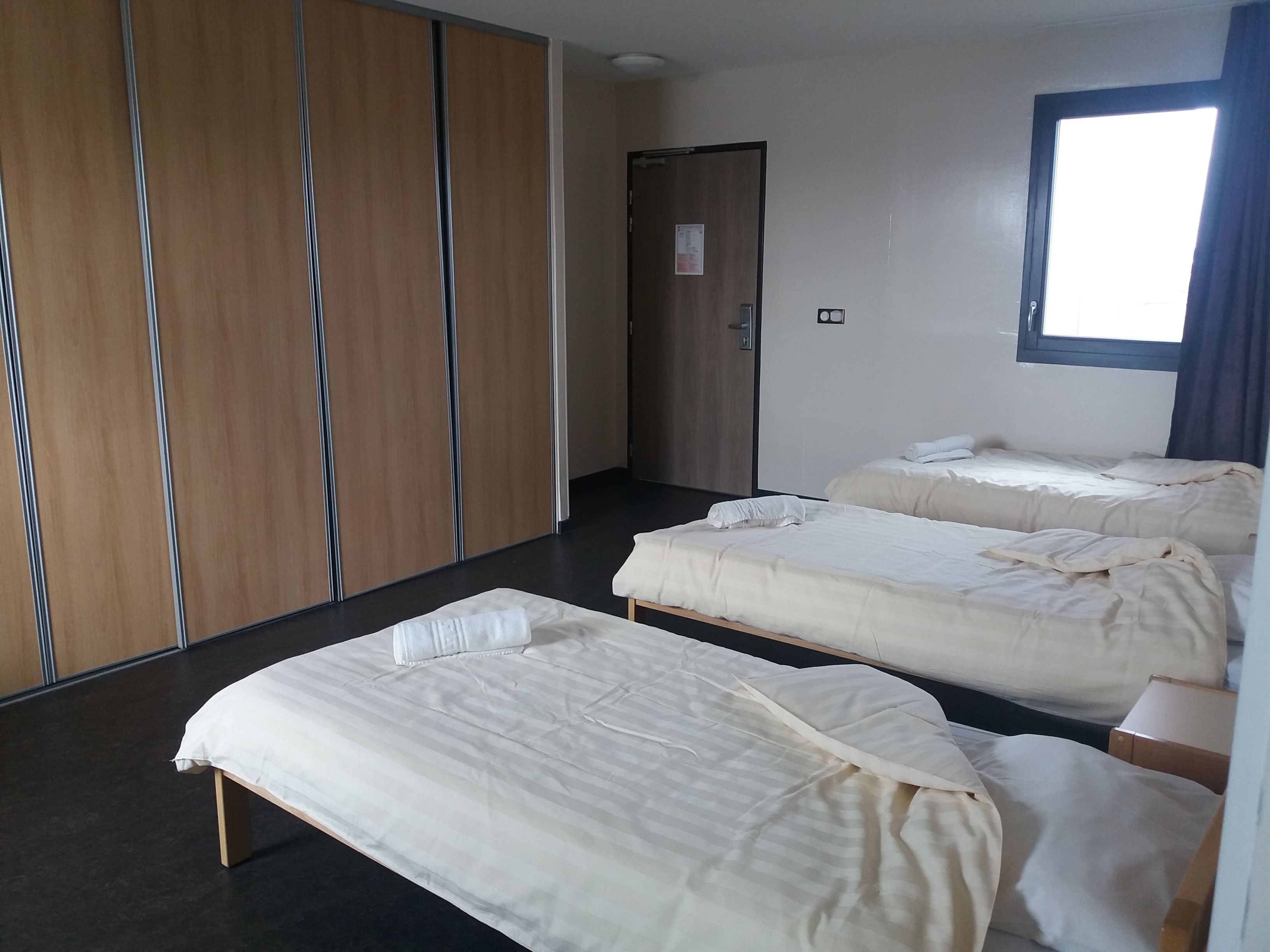 A hotel room with two beds, a wardrobe, a door, and a window.
