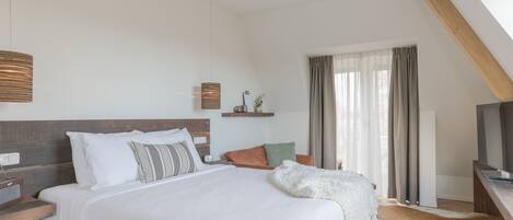 Un dormitorio moderno con una cama grande, cabecera de madera, mesita de noche con radio, televisor y ventana con cortinas.
