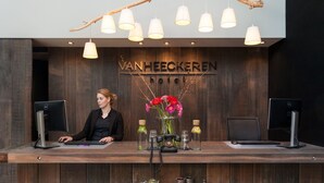 A reception desk with two monitors, a woman seated behind it, and a sign above reading "VANHEECKEREN." - Van Heeckeren Hotel (Nes)