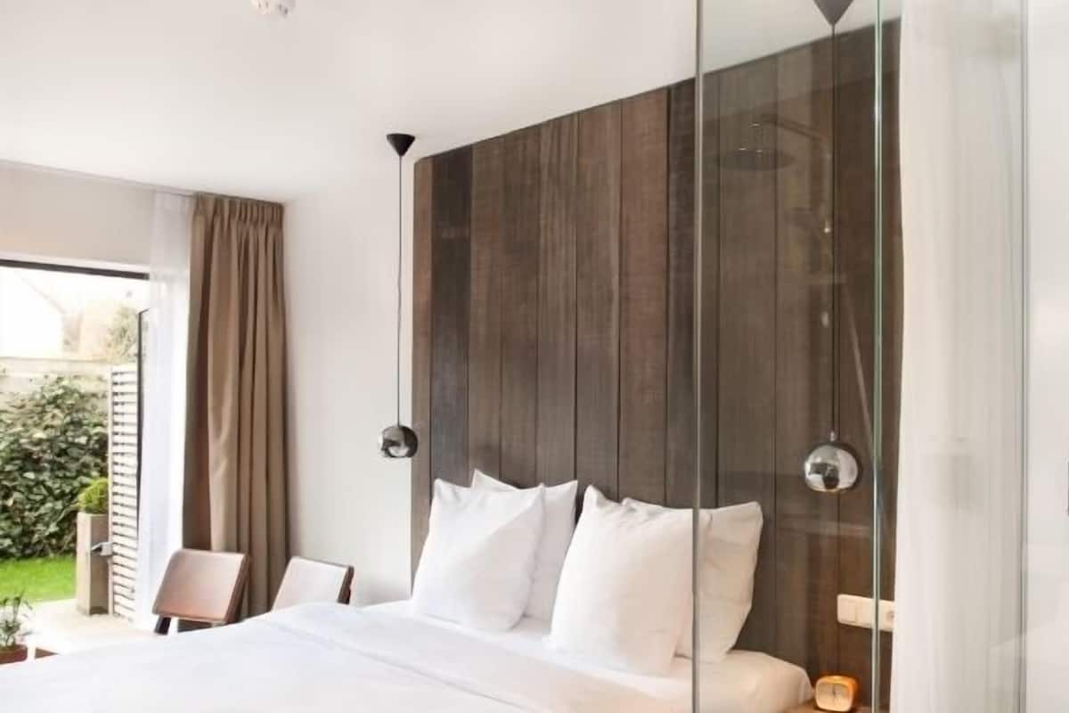 Une chambre d’hôtel moderne dotée d’un grand lit, d’une douche à parois de verre et offrant une vue sur l’extérieur.