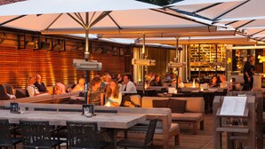 An outdoor seating area with tables and chairs, a bar, and a fire feature. - Van Heeckeren Hotel (Nes)