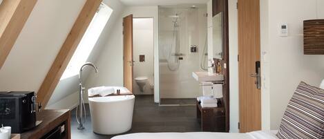 A modern hotel room with a large bed, a bathtub, a shower, and a separate bathroom.