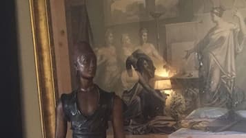 Una estatua de una mujer sosteniendo dos mancuernas en una habitación con un cuadro en la pared.