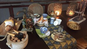 Uma mesa posta com diversos pratos, incluindo pão, nozes e um prato com o que parece ser um doce. Há também objetos decorativos como um bule e um castiçal.