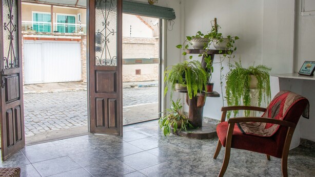Puerta abierta que da a un patio con suelo de baldosas, una silla de madera y varias plantas en macetas.