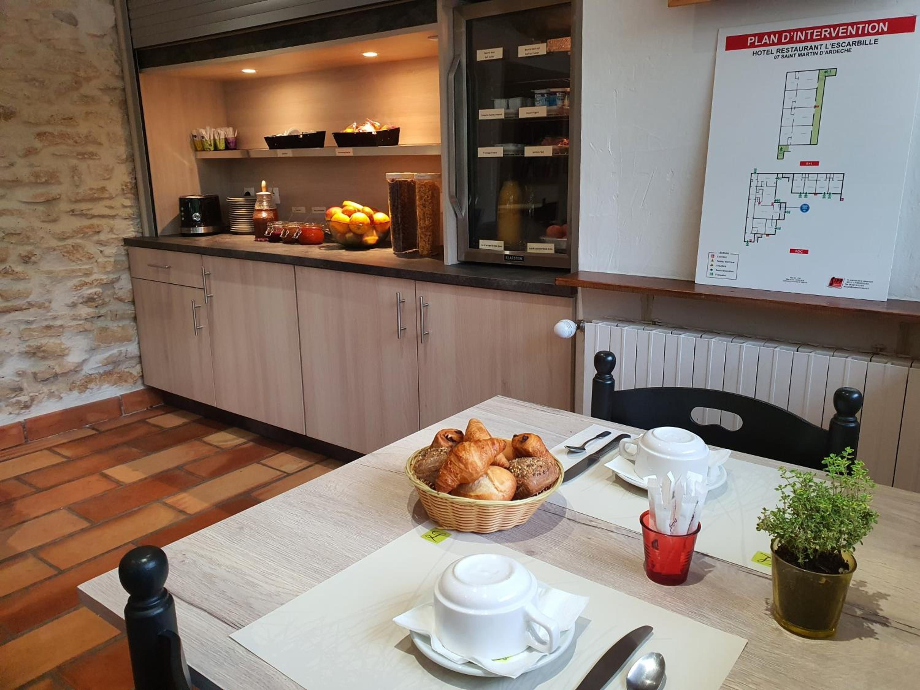 Una mesa con bollos, una taza de café y una taza roja, con una cocina visible al fondo.