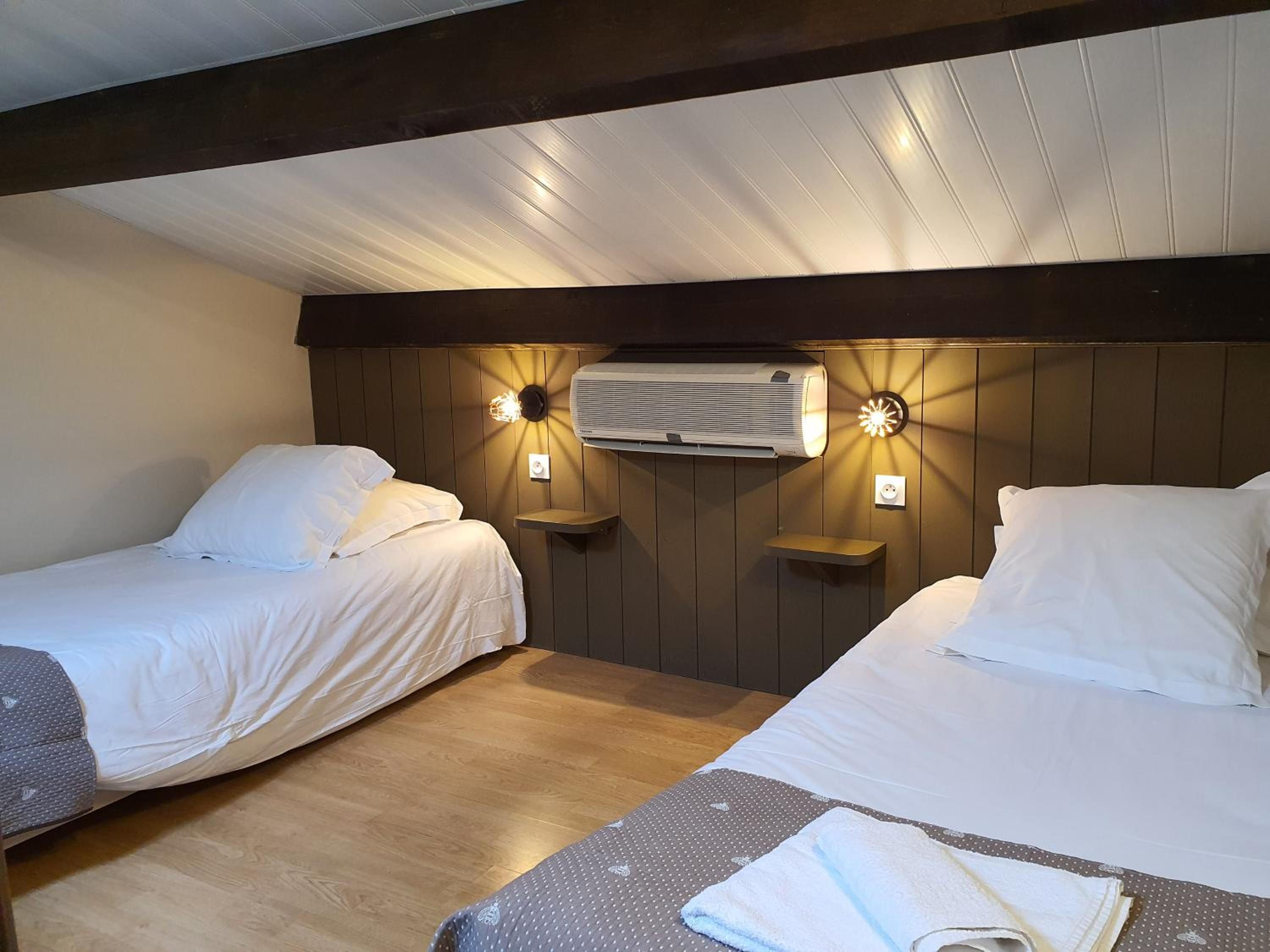 A hotel room with two beds, wooden paneling, wall-mounted air conditioning, and bedside lamps.