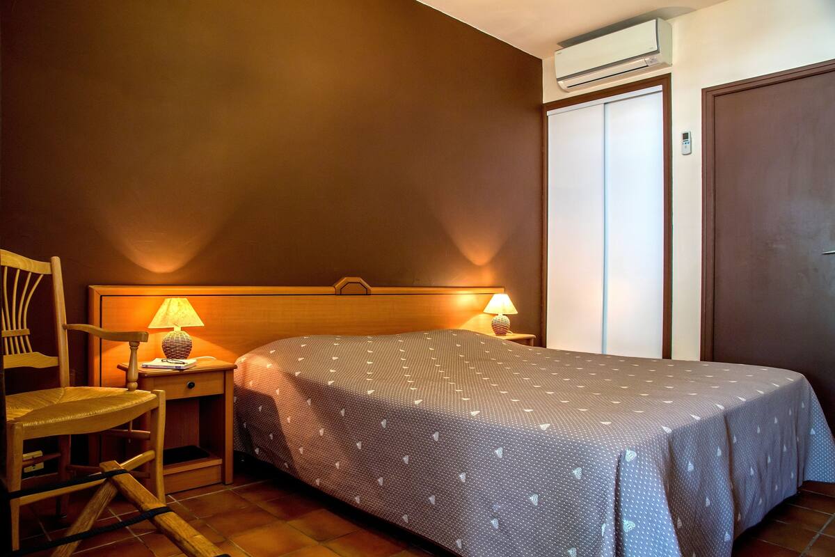 Ein Hotelzimmer mit einem Bett, einem Sessel, einem Nachttisch mit Lampe und einem Kleiderschrank.