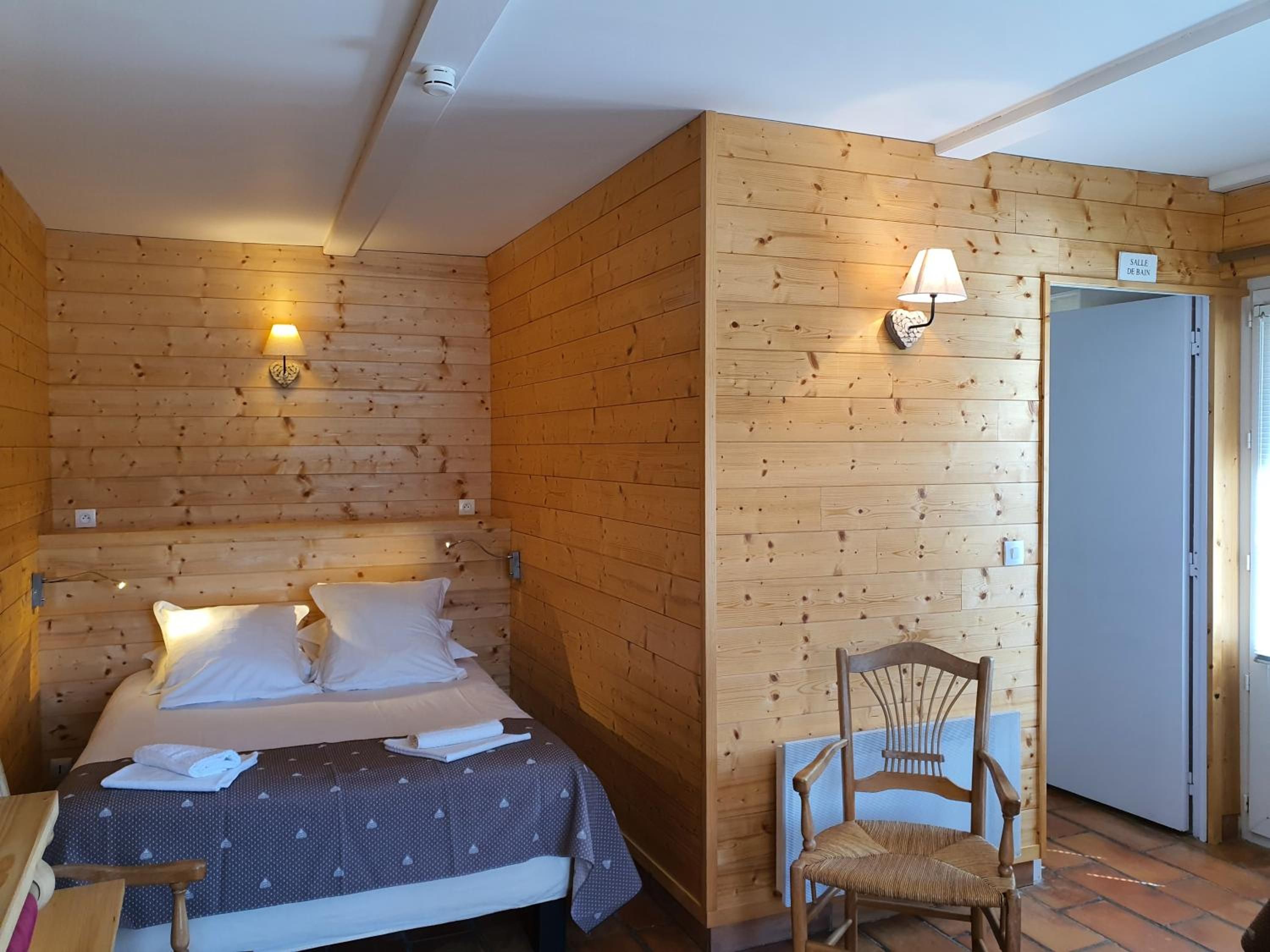 Een kamer met houten lambrisering, een bed, een stoel en een deur met de tekst 'SALLE DE BAIN'.