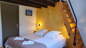 Un dormitorio con techo inclinado de madera, una cama con ropa de cama blanca, una mesita de noche con una lámpara y una escalera de madera.