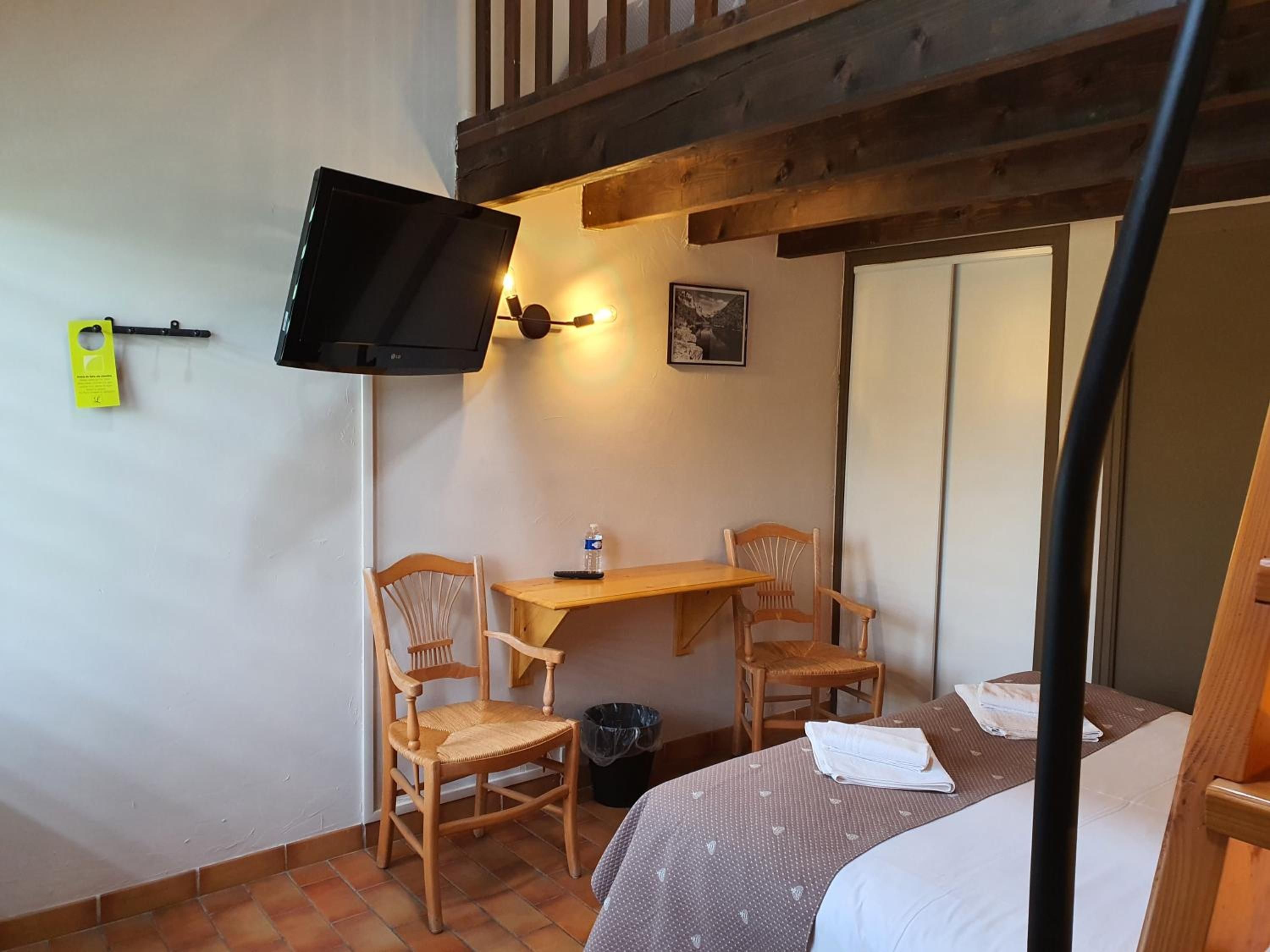 Een kamer met een bed, een bureau met stoel, een aan de muur bevestigde televisie en een kleine prullenbak.