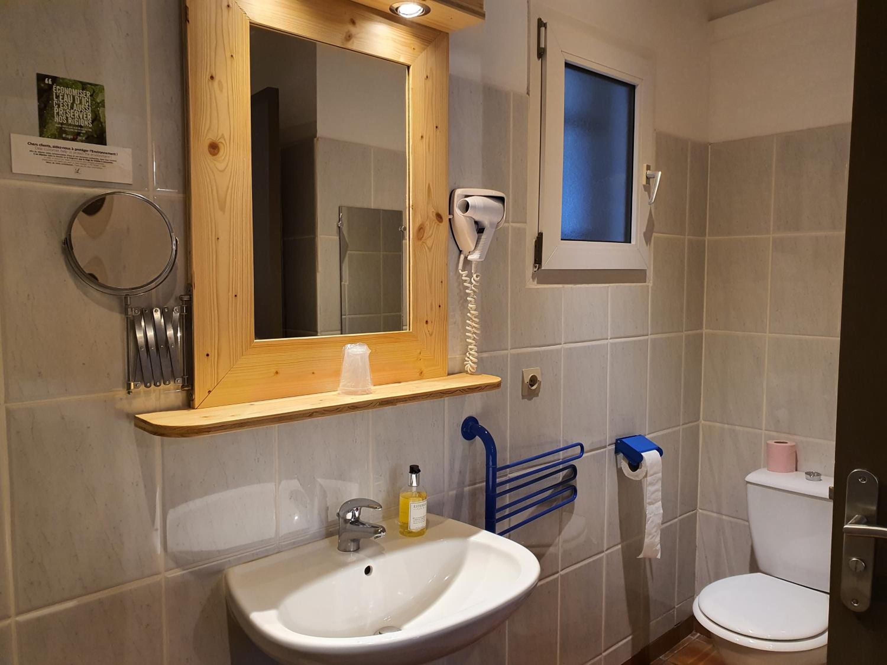 Un baño con espejo de marco de madera, lavamanos, inodoro y secador de pelo.