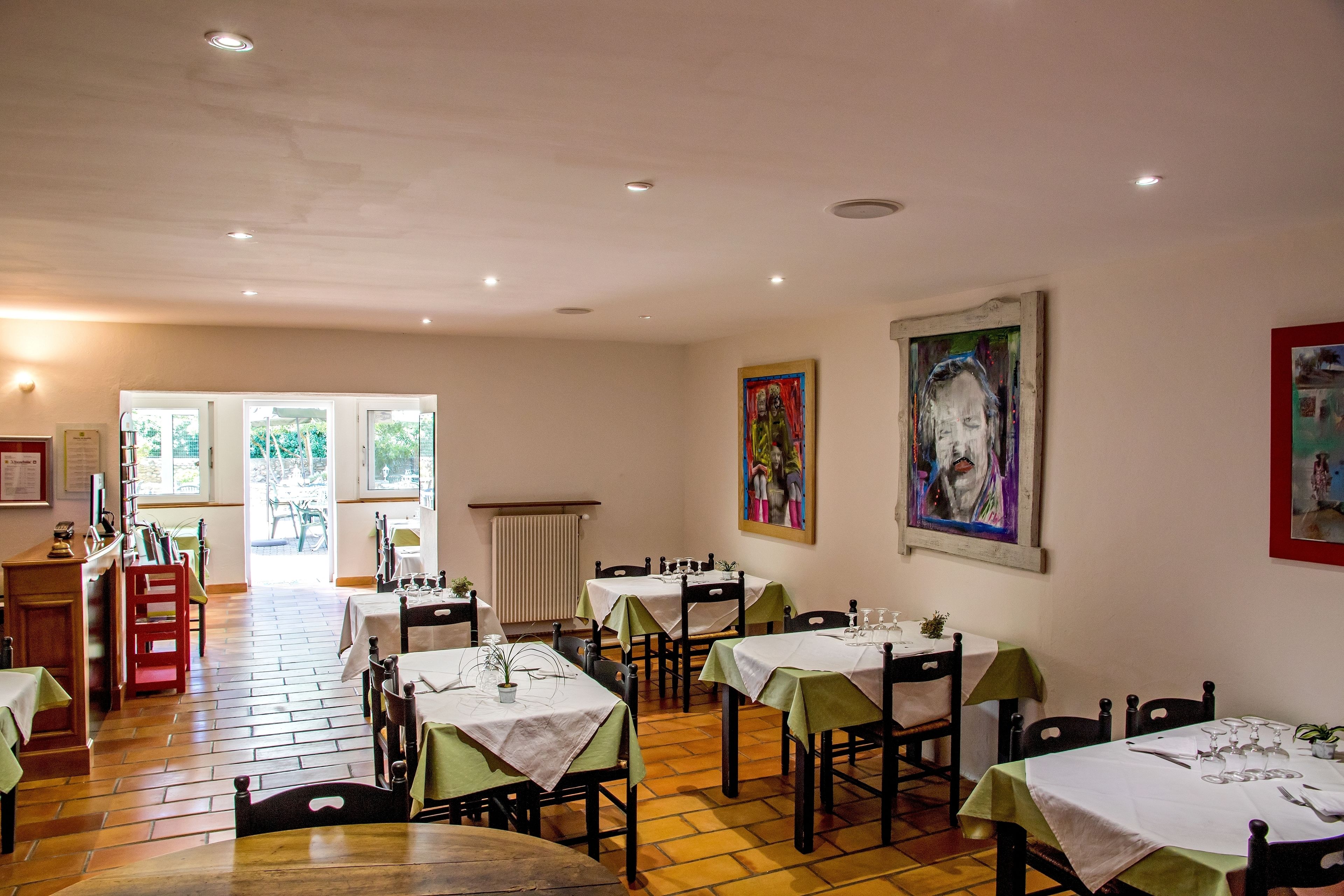 Un comedor con mesas dispuestas para el servicio, sillas de madera y obras de arte en las paredes.