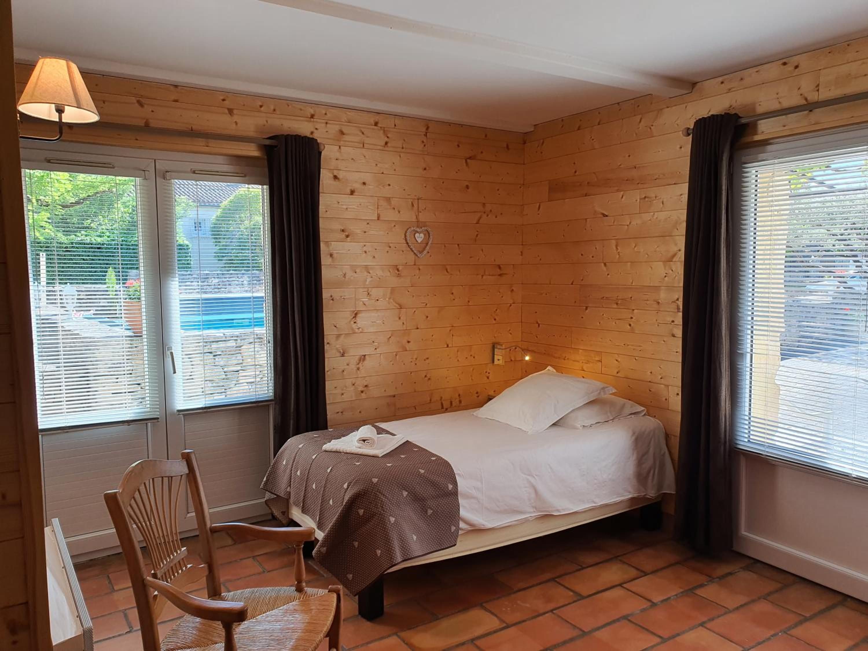 Ein Zimmer mit Holzwänden, einem Bett, einem Sessel und einem Fenster mit Jalousien.