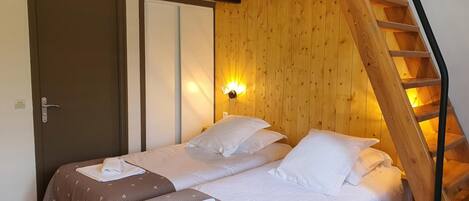 A room with two beds, a wooden staircase, and a wall-mounted light fixture.