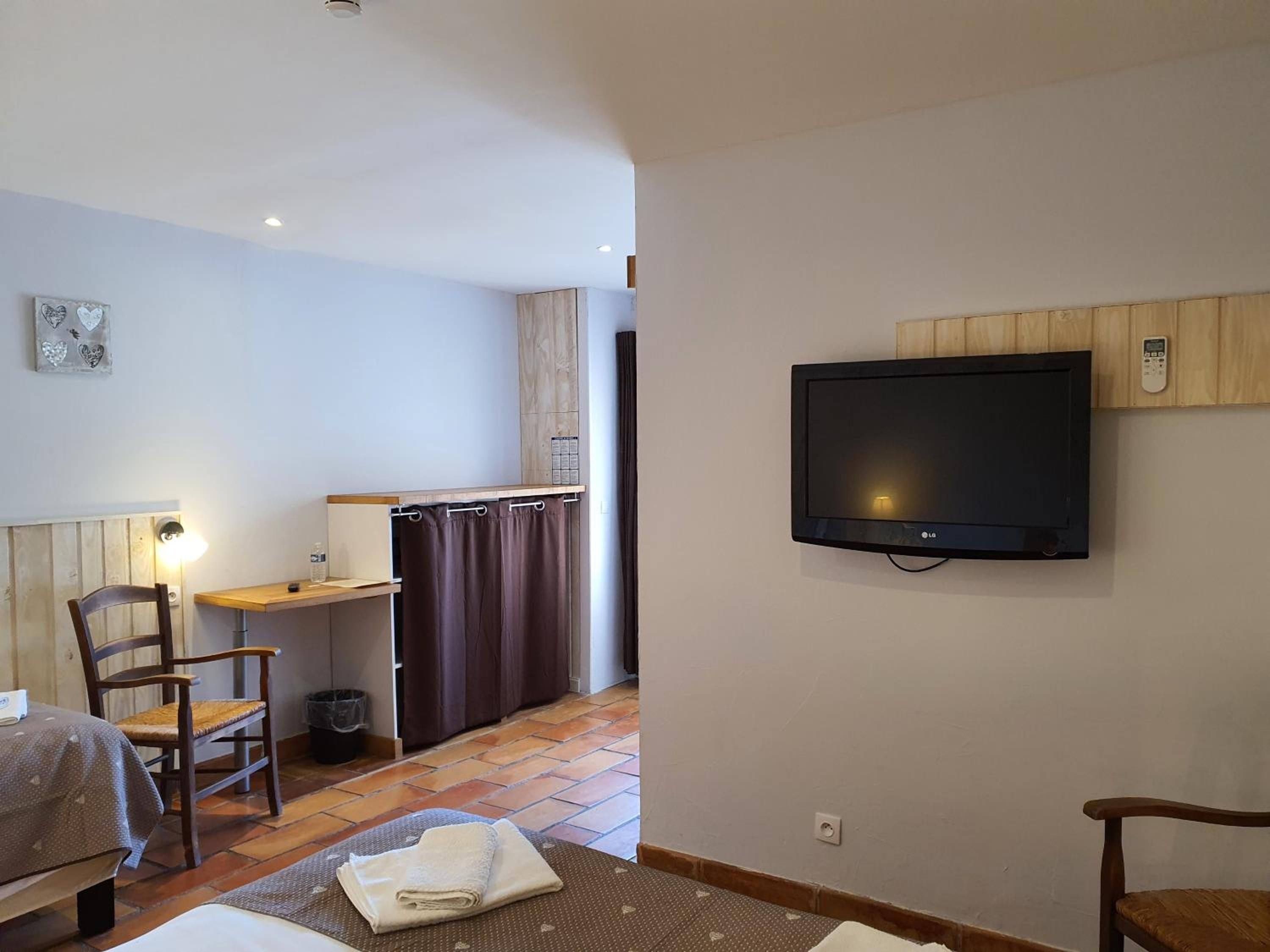 Ein Hotelzimmer mit einem Bett, einem Sessel, einem Schreibtisch, einem an der Wand befestigten Fernseher und einem kleinen Tisch.