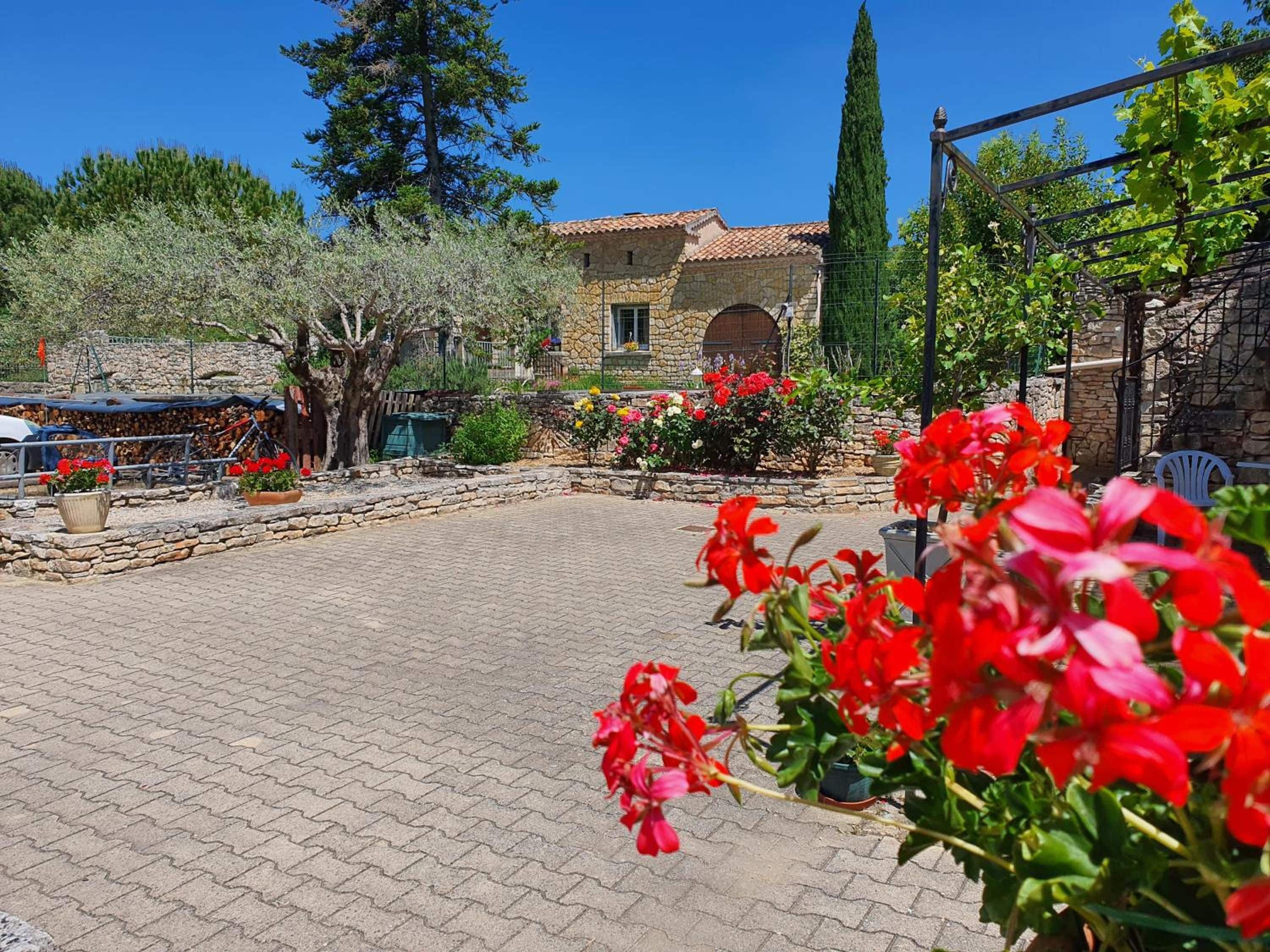 Un patio con pavimento de piedra, un edificio de piedra con techo de tejas y diversas macetas con plantas y flores.