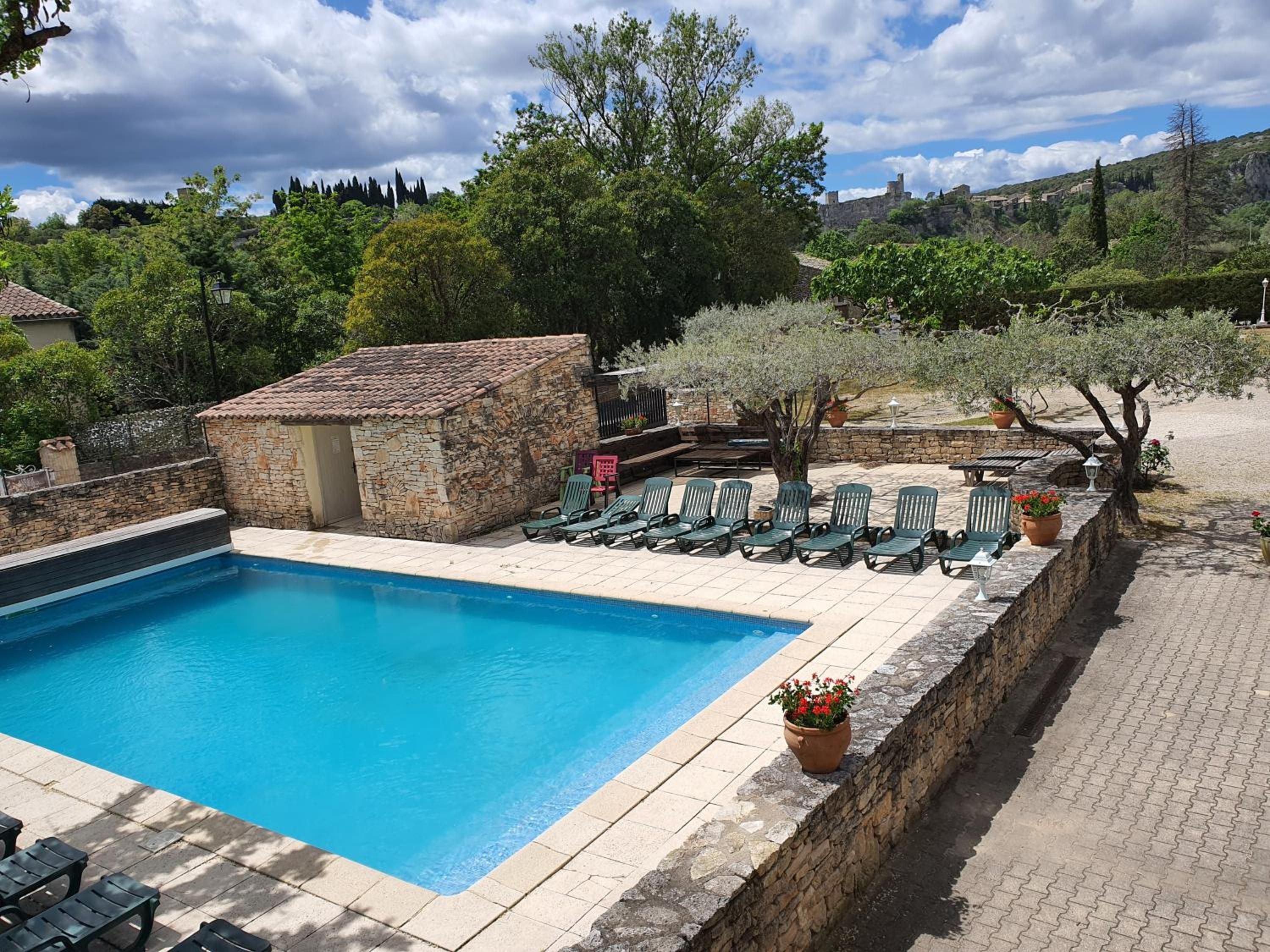 A swimming pool with lounge chairs and a stone building, surrounded by trees and hills.