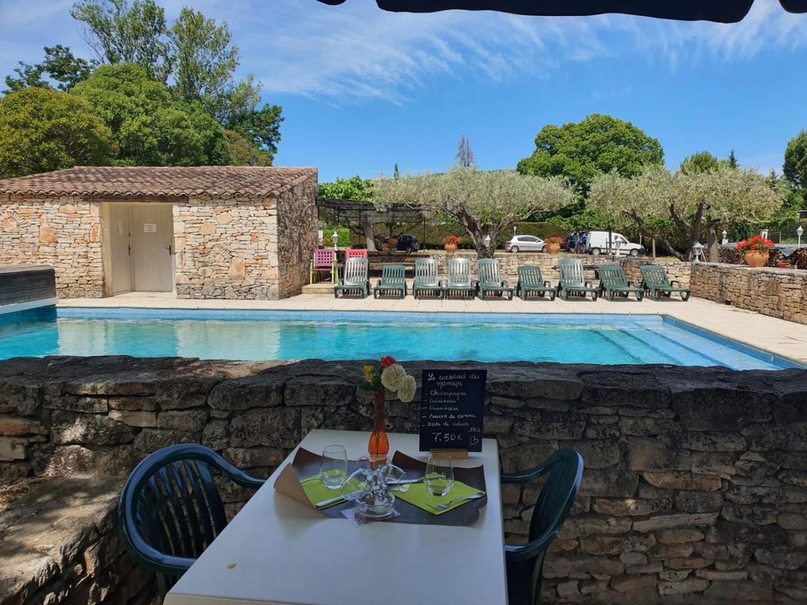 A poolside dining area with a stone wall, a table with a menu, and green chairs.