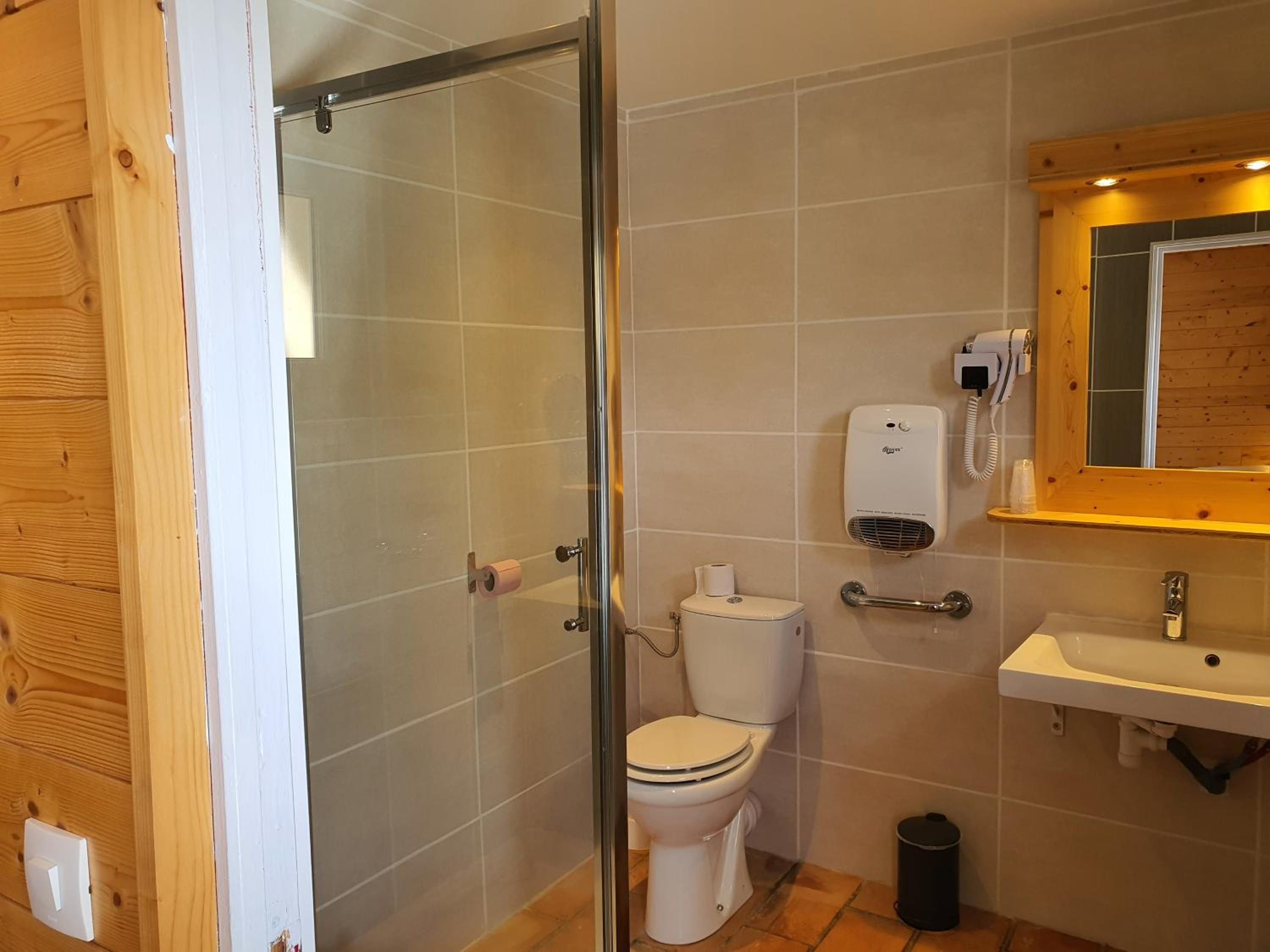 A bathroom with a glass shower enclosure, a toilet, a hand dryer, and a sink.