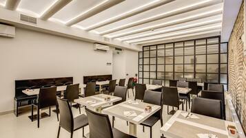 A modern dining area with multiple tables and chairs, a large window with a view, and a unique ceiling design.