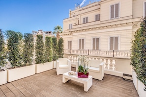 Una terraza en la azotea con un sofá blanco, una mesa de centro de vidrio y plantas en macetas.