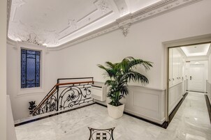 A grand hallway with a marble staircase, a large potted plant, and a decorative window.
