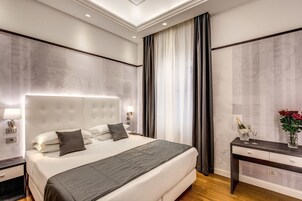 A modern hotel room with a large bed, a bedside table with a vase of flowers, and a nightstand with a lamp.