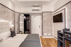 A modern hotel room with a large bed, a walk-in closet, a flat-screen TV, and a minibar.